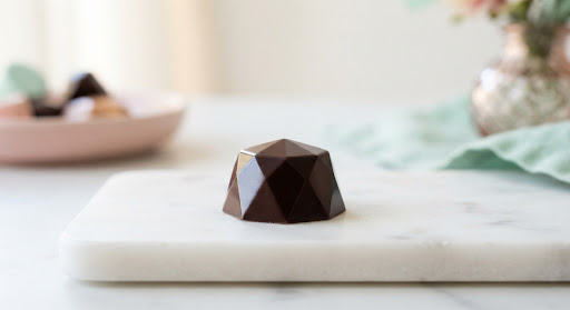 A faceted dark chocolate truffle photographed on white marble.