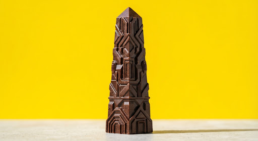 An obelisk-shaped chocolate bar with brutalist patterns on a yellow background.