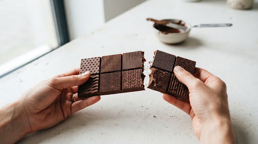 A modular chocolate bar with varied geometric textures being snapped apart.