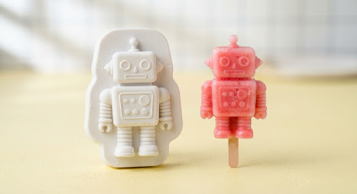 White robot ice pop mold beside a strawberry-pink robot ice pop.